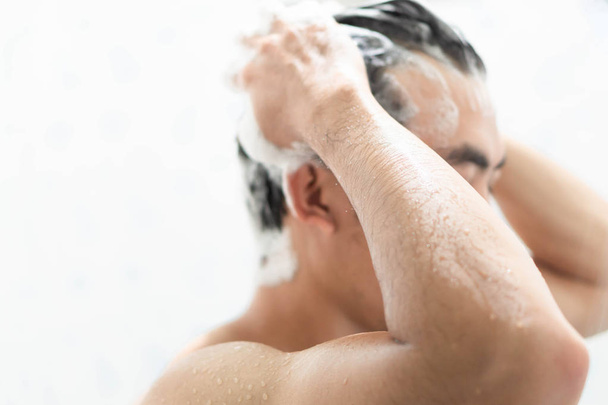 Nahaufnahme junger Mann beim Haarewaschen mit Shampoo im Badezimmer, Gesundheitskonzept, selektiver Fokus - Foto, Bild
