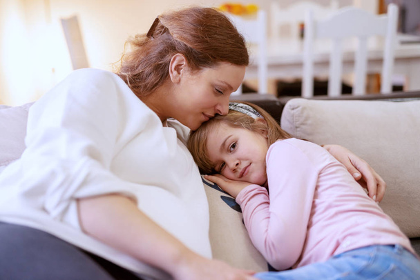 Bella mamma caucasica incinta sdraiata sul divano in soggiorno e rilassante con la sua graziosa figlia
. - Foto, immagini
