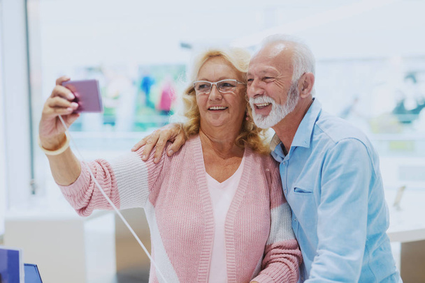 Чарівні посміхаючись кавказька старша пара беручи селфі в Tech Store. - Фото, зображення