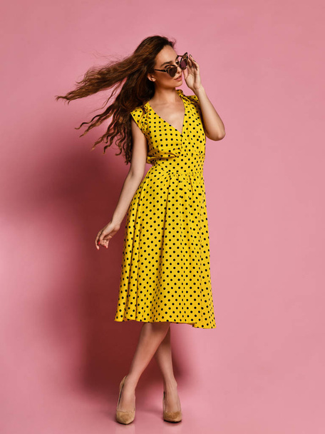 Beautiful girl in a romantic dress smiling pretty on a purple background. Slender curly female model in a yellow polka dot dress - Photo, image