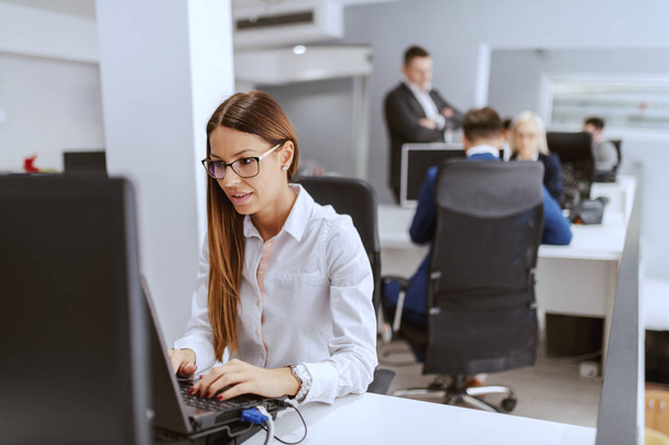 engagierte, hochmotivierte Geschäftsfrau, die am Arbeitsplatz sitzt und den PC nutzt. Hände auf der Tastatur. im Hintergrund ihre Kollegen bei der Arbeit. - Foto, Bild