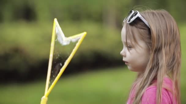 Zelfverzekerde speelse kleine schattige meid waait enorme lucht zeep Bubble blower medium close-up - Video