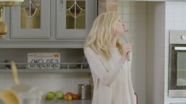 Plavovlasá žena v kuchyni tančí a zpívá kuchyňským nádobí jako mikrofon - Záběry, video