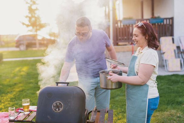 Immagine di coppia di mezza età che fa barbecue nel loro cortile. Pranzo in famiglia nella giornata estiva. - Foto, immagini