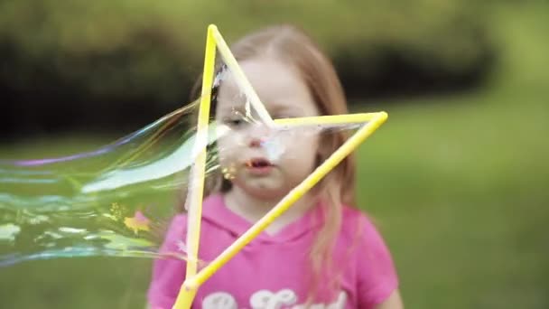 Confiado juguetón pequeña linda chica soplando enorme jabón de aire burbuja soplador medio primer plano
 - Metraje, vídeo