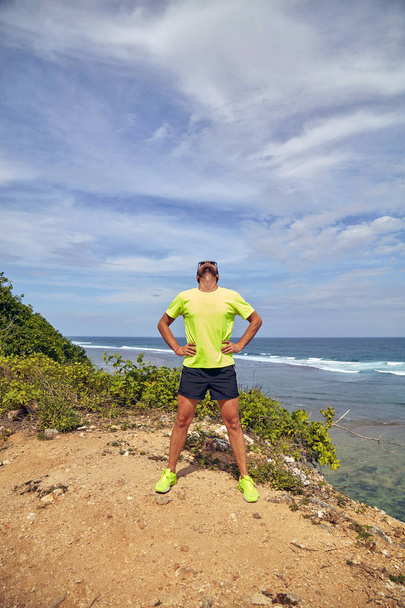 Deportista estirándose en un acantilado tropical exótico cerca del océano
. - Foto, imagen
