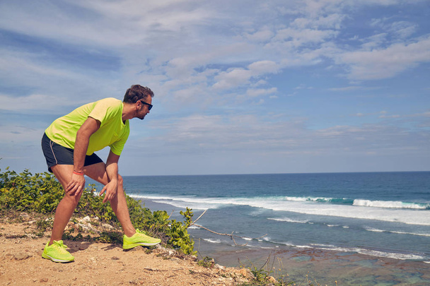 Sportsman stretching on a tropical exotic cliff near the ocean. - Zdjęcie, obraz