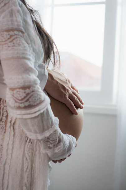 Mann benutzt Hand, um Bauch der schwangeren Frau in weißem Kleid zu berühren - Foto, Bild