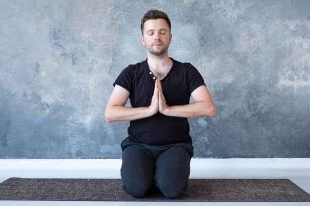 Young sporty man practicing yoga lesson sitting in vajrasana pose - 写真・画像