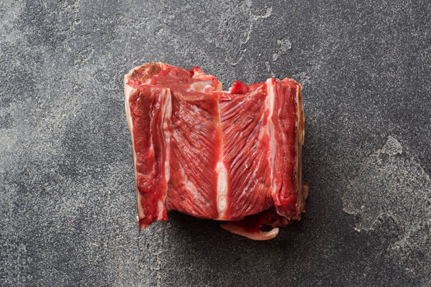 Fresh raw piece of beef rib with meat on a dark concrete background with copy space. - Фото, зображення