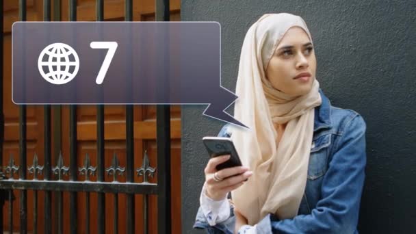 Ψηφιακή σύνθεση της γυναίκας στη μαντίλα που γέρνει σε έναν τοίχο κοντά σε μια πύλη ενώ στέλνει μηνύματα. Δίπλα της είναι ένα εικονίδιο ειδοποιήσεων με αυξανόμενη καταμέτρηση για τα μέσα κοινωνικής δικτύωσης - Πλάνα, βίντεο