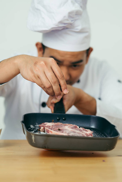 Chef spreading black peppers on meat for preparing food. - Zdjęcie, obraz
