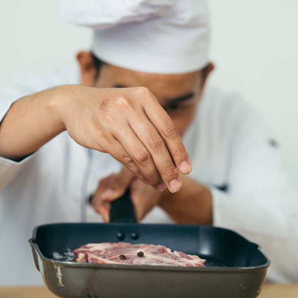 Chef spreading black peppers on meat for preparing food. - Photo, image