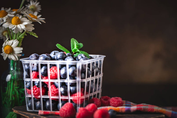 Raspberries and blueberry in a basket on a dark background. Summer and healthy food concept. Background with copy space. Selective focus. - Photo, Image