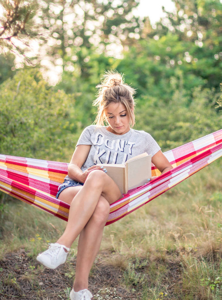 junge attraktive kaukasische Frau liest Buch in Hängematte im Wald, Sonne auf dem Hintergrund - Foto, Bild