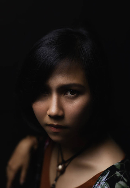 Asiática mujer de pelo negro corto El uso de joyas de cuero y piedra En su cara, hay una pequeña peca En un fondo negro y sombras
 - Foto, Imagen