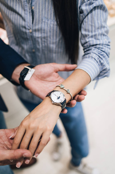 Beautiful couple enjoying in shopping at modern jewelry store. Close up shot of human hand holding expensive watch. - Foto, imagen