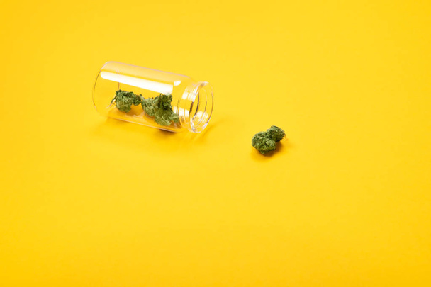 Dry medical cannabis buds in a glass bottle on yellow background.  - Foto, afbeelding