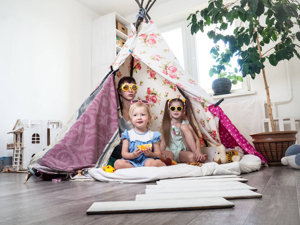 Perhe-aika: Äiti ja jotkut sisaret lapset leikkivät kotona lasten kotitekoisessa teltassa
. - Valokuva, kuva