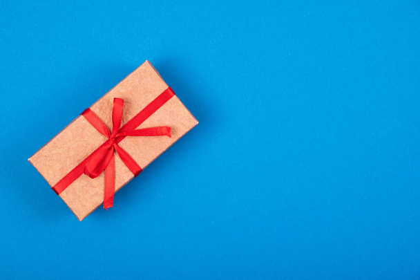 Κουτί δώρου με κόκκινη κορδέλα και τόξο σε κυανό μπλε φόντο.  - Φωτογραφία, εικόνα