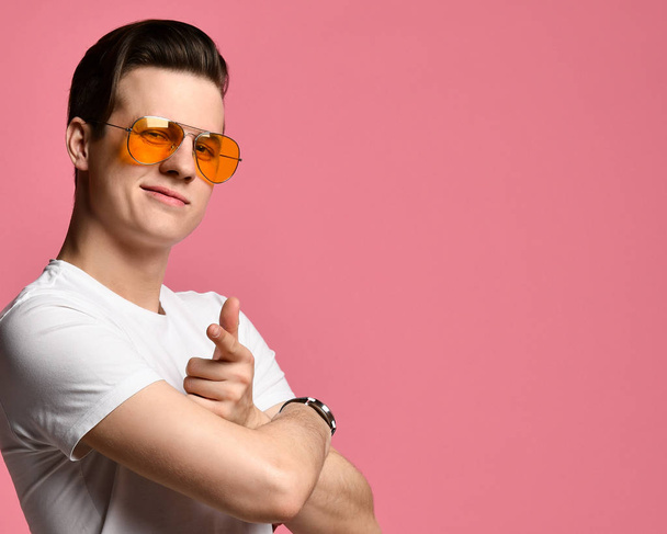 Portrait of a fashionable, brunette, cute, positive guy in a white T-shirt pointing his index fingers at you - Foto, Imagem