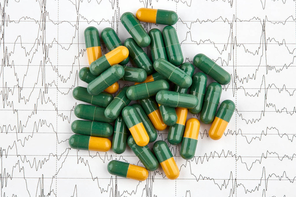 Nahaufnahme vieler grüner und gelber Pillen auf ekg-Grafik - Foto, Bild