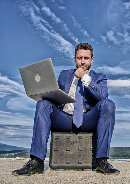 Laptop indispensable attribute modern businessman. Modern technologies portable device opportunity work worldwide. Business on fresh air. Businessman with laptop sit briefcase blue sky background - Foto, immagini