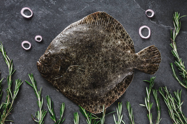 Surowe całe ryby flątwy z rozmarynem, cebulą i przyprawami na ciemnym - Zdjęcie, obraz