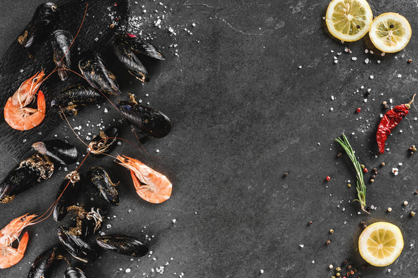 Verse rauwe mosselen en garnalen met specerijen en citroen op donkere steen - Foto, afbeelding