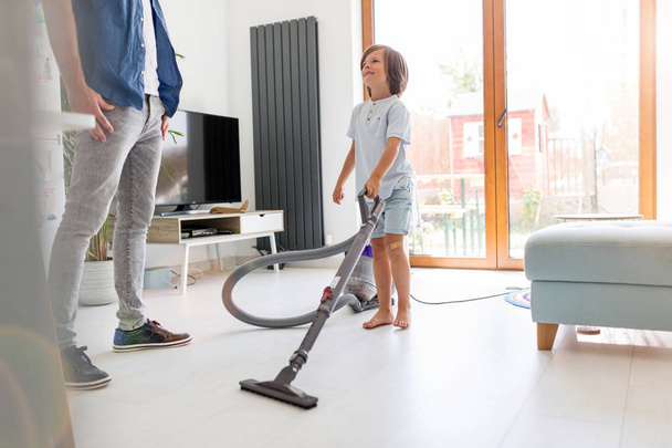 Boy vacuuming floor while father standing at home - Fotografie, Obrázek