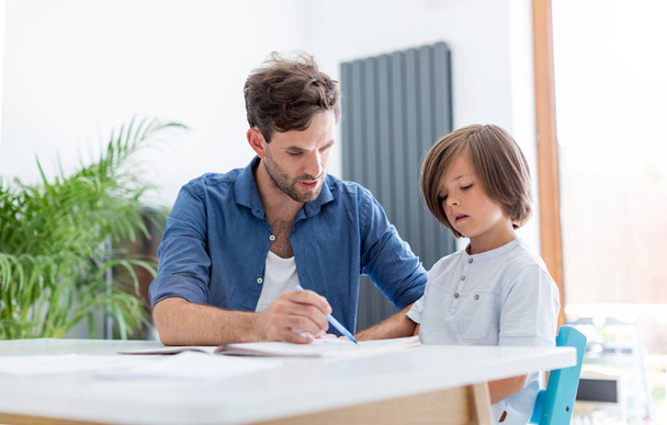 Father and son doing homework together at home - Фото, изображение