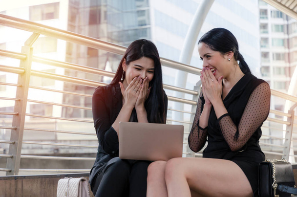 two young beautiful business woman team feeling excited surprised and looking graph chart on laptop computer and sitting on stairs in modern city, investor, investment, financial and emotion concept - Foto, Bild