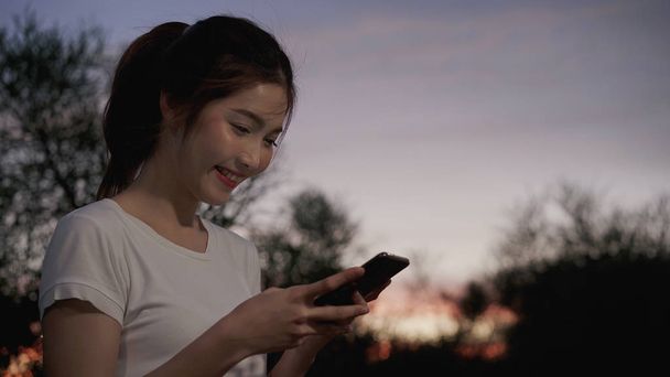 Wesoły turystycznych Azji kobieta blogger za pomocą technologii ekranu dotykowego o smartphone podczas spaceru na ulicy, w centrum miasta w nocy. Styl życia plecak turystyczny travel wakacje koncepcja. - Zdjęcie, obraz