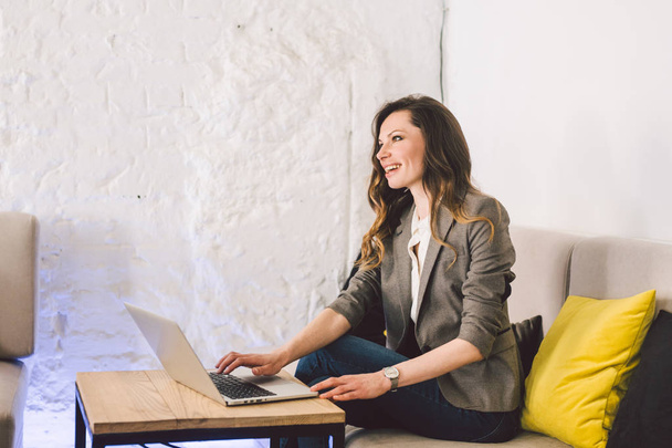 Concentrated at work. Confident young adult middle-aged woman in smart casual clothes, working on a laptop, sitting inside a creative office or cafe. Theme business woman work in free space - Foto, Bild