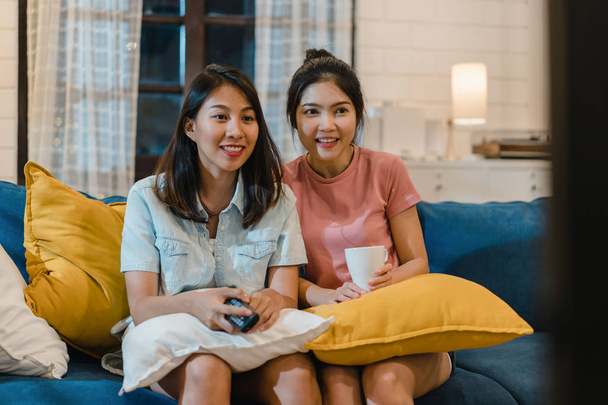 Lesbian lgbt women couple watching television at home, Asian female lover feeling happy funny moment looking drama entertainment together on sofa in living room in night concept. - Photo, image
