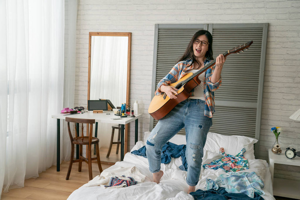 girl jumping whilst playing guitar on bed - Foto, Bild