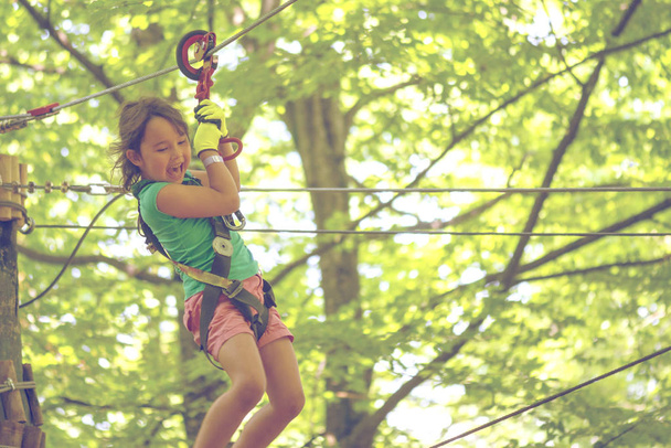 Joyeux petite fille sur tyrolienne entre les arbres
 - Photo, image