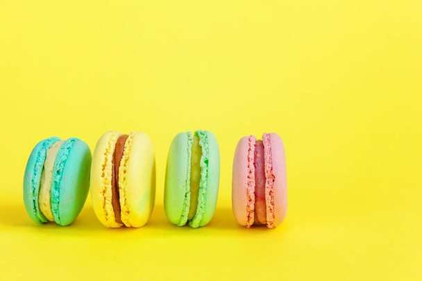 フランスの甘いクッキー。最小限の食べ物ベーカリー コンセプト。黄色の背景にピンク青黄色緑マカロン - 写真・画像