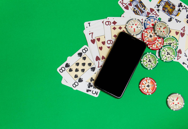 mobile phone and poker chips with playing cards on a green table - Photo, Image