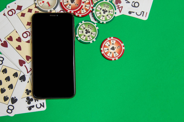 緑色のテーブルの上にトランプと携帯電話とポーカーチップ - 写真・画像