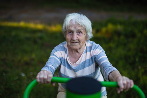 Μια ηλικιωμένη γυναίκα άσκηση στην παιδική χαρά του δρόμου. Υγεία των ηλικιωμένων. - Φωτογραφία, εικόνα