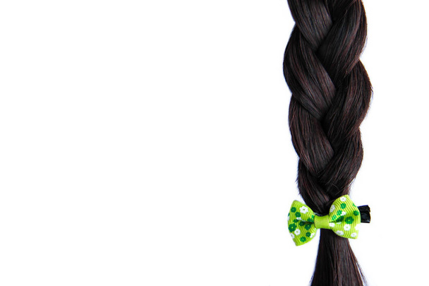 白い背景に隔離された緑の弓を持つ黒い暗い編組ヘア。白い背景に緑の髪のピンとブルネット自然編組ヘアエクステンション - 写真・画像