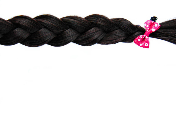 Μαύρο σκούρο μαλλιά πλεγμένο με ροζ τόξο απομονώνεται σε λευκό φόντο. Μελαχρινή φυσική επέκταση τρίχας με ροζ τσιμπιδάκι σε λευκό φόντο - Φωτογραφία, εικόνα