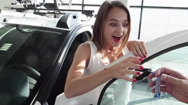 Happy young woman enjoying her first car at car showroom, slow motion  - Záběry, video