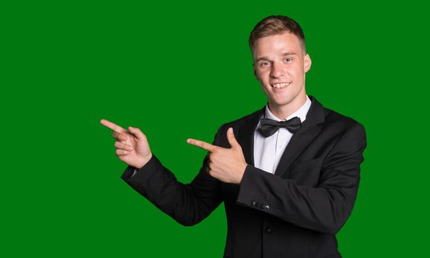 Handsome man in suit points his fingers left isolated on green background. - Photo, Image