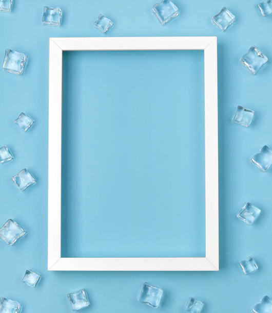 Plana maqueta con marco blanco y cubitos de hielo sobre fondo azul
. - Foto, Imagen