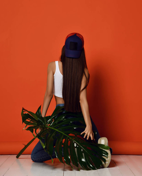 Young woman in blue teenage cap hat with tropical leaves backside rear view on orange - Foto, immagini