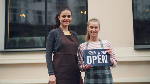 Portrait of beautiful girls standing outdoors with we are open sign smiling - Footage, Video