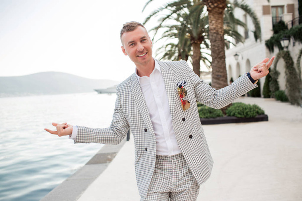 Stylish businessman is wearing white fashion costume stands on the background of the bay with luxury yachts. Montenegro bay. - Photo, image