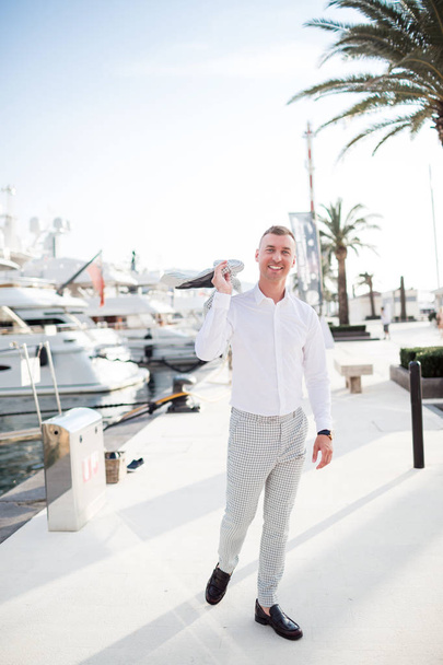 Stylish happy businessman is wearing white fashion costume stands on the background of the bay with luxury yachts. Montenegro bay. - Foto, Imagem